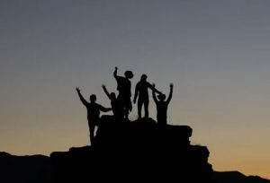 A silhouette of a team on top of a mountain