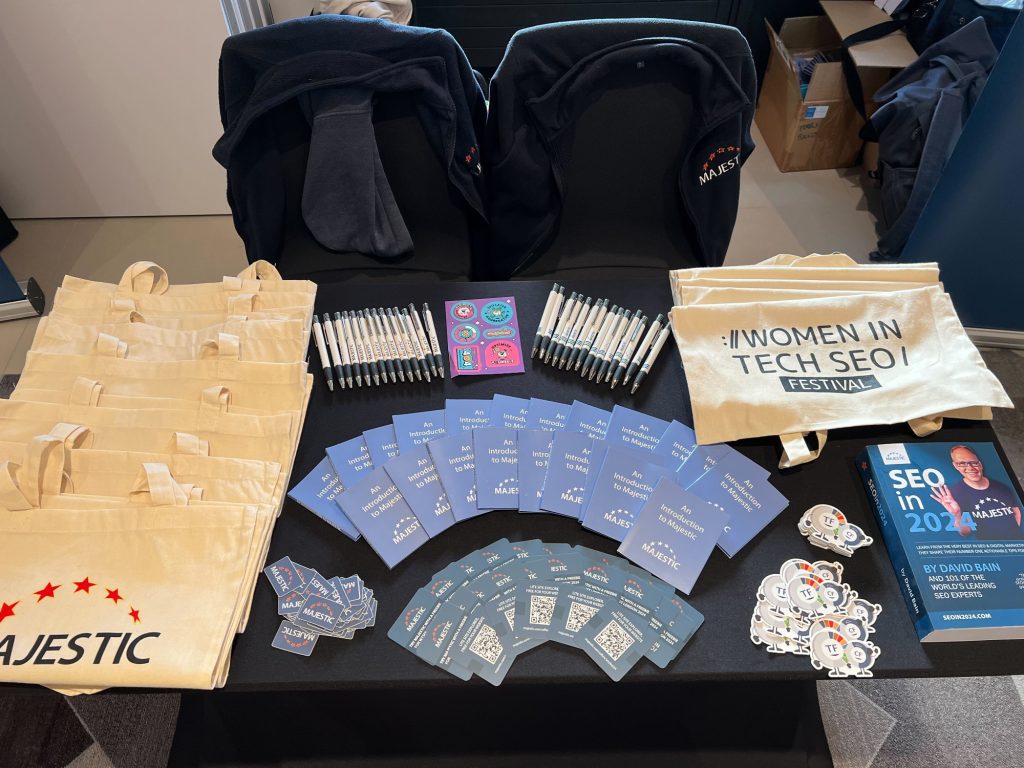 The Majestic stand at WTSFest with an assortment of Women In Tech SEO Festival & Majestic co-branded tote-bags, stickers, pens, and a copy of SEOin2024.